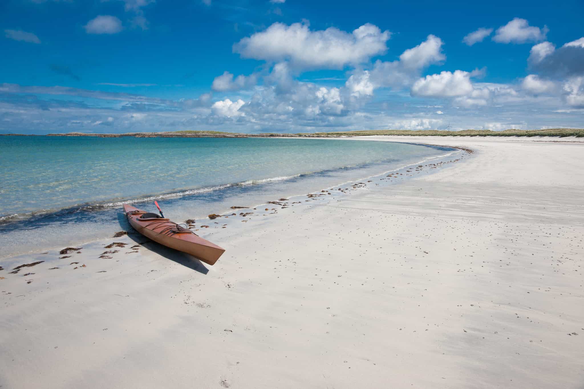 Single kayak on a deserted white sand beach in Scotland.