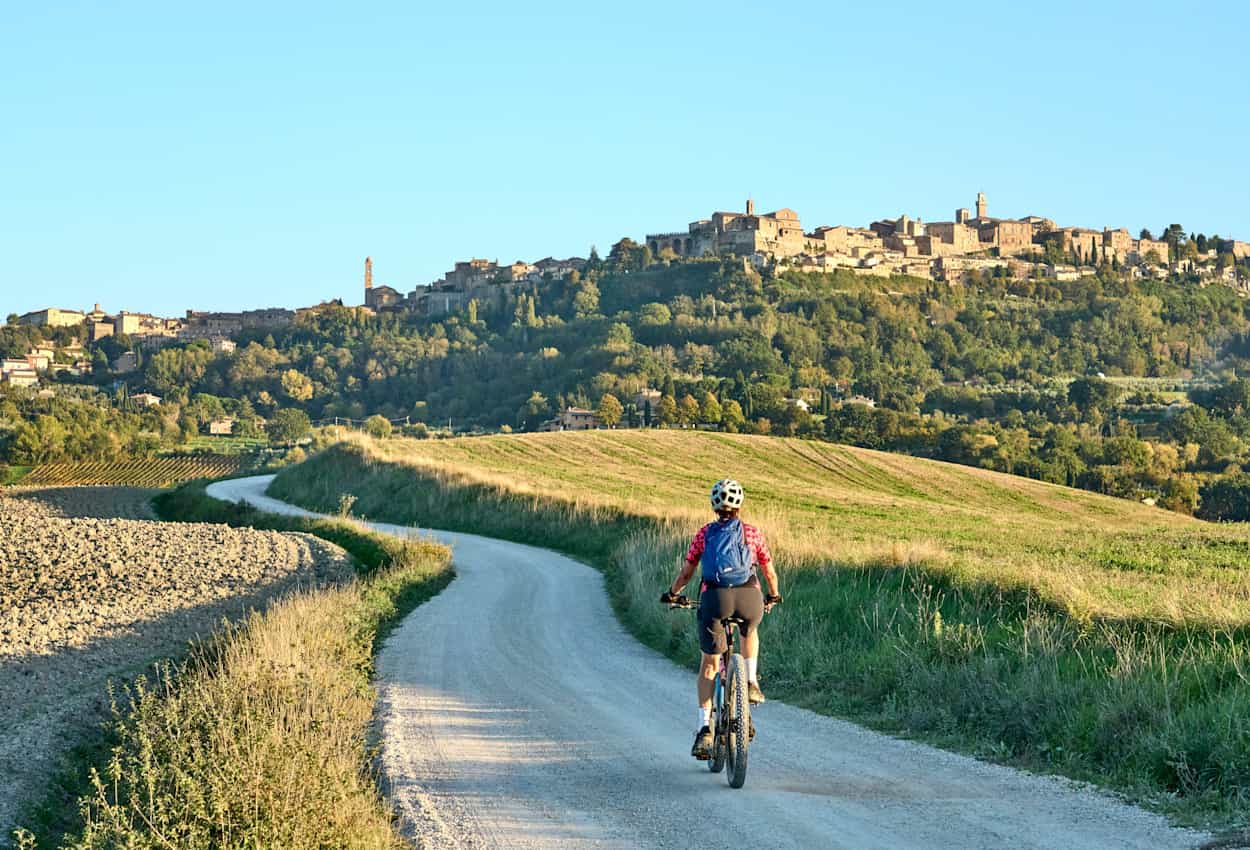 Woman riding her electric mountain bike between olive trees with Montepulciano in background, Tuscany , Italy.