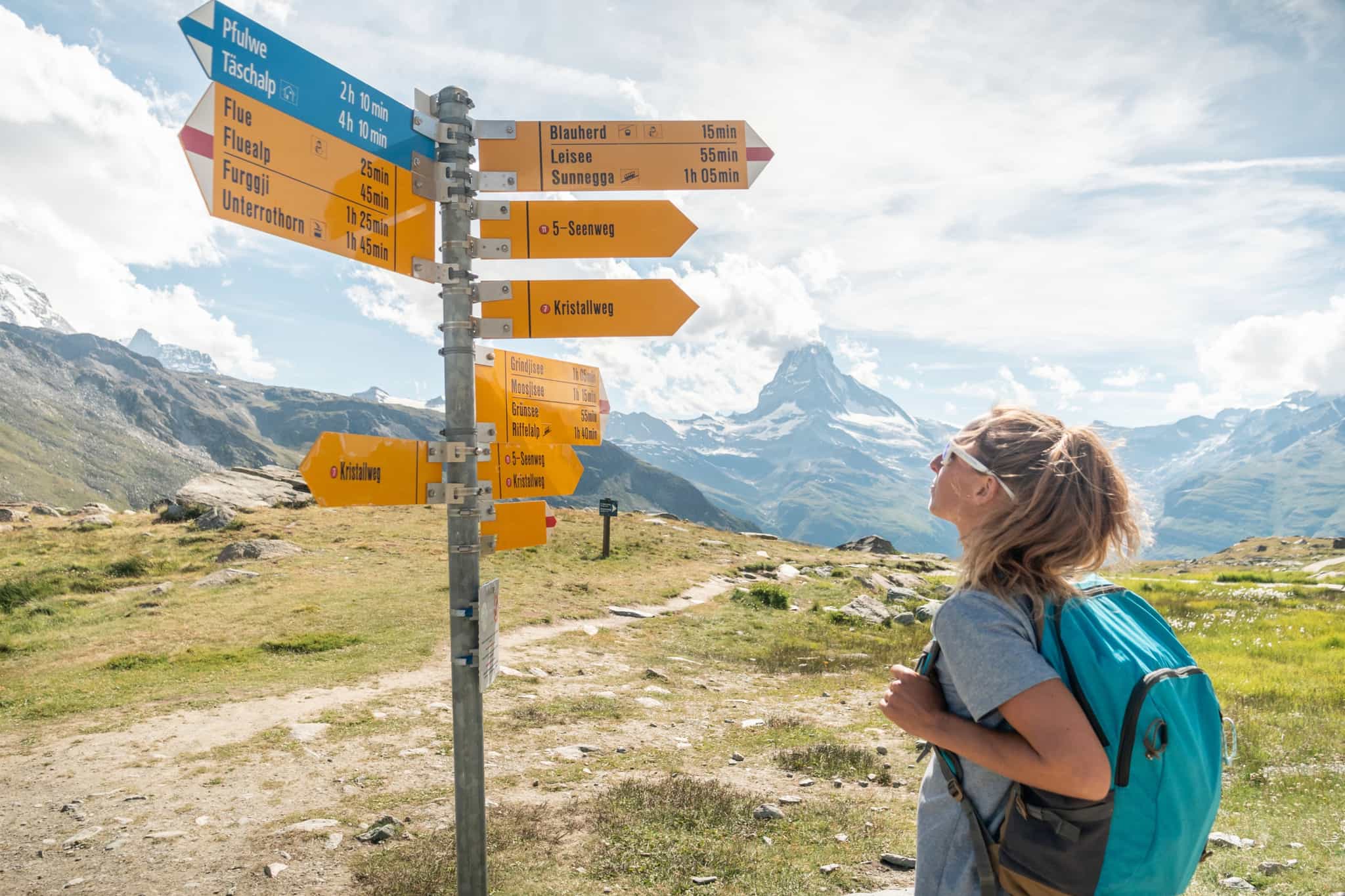 Hiker looks at a trail sign with Matterhorn behind.