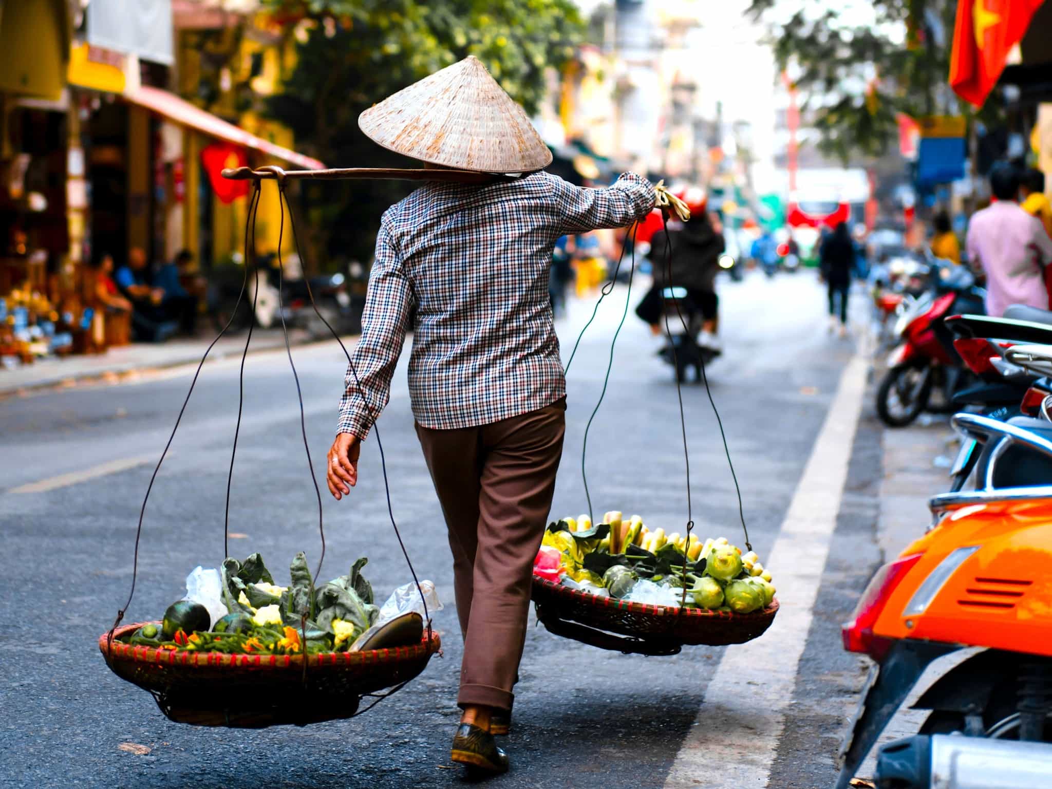 Person with a traditional Vietnamese hat carrying baskets in Hanoi, Vietnam.