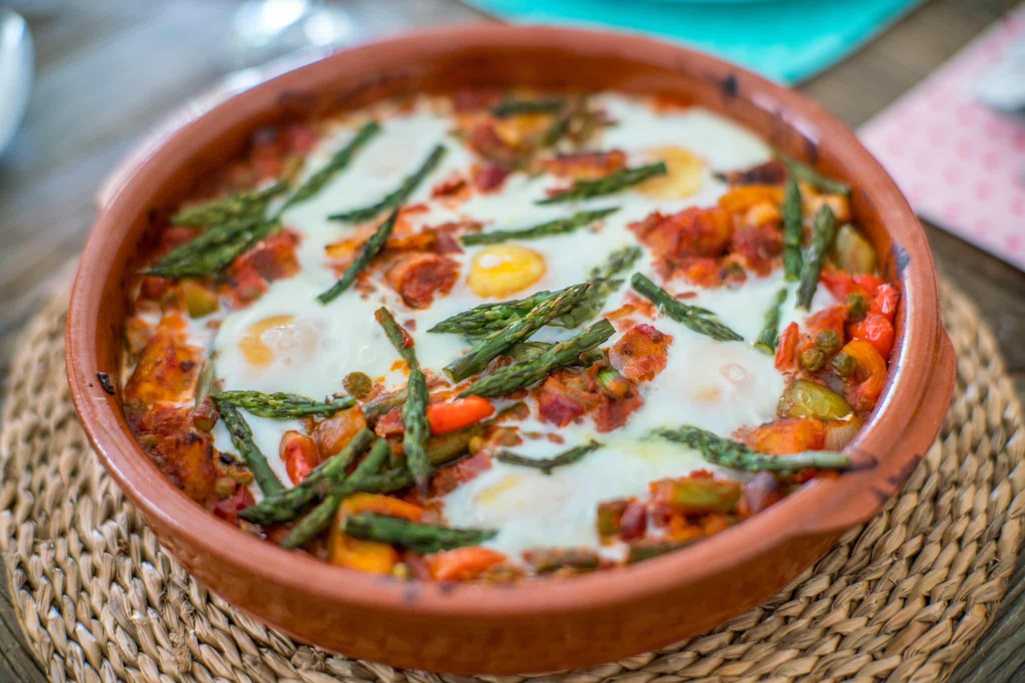 Huevos a la flamenca, served in a clay pot with asparagus, peppers, and tomatoes